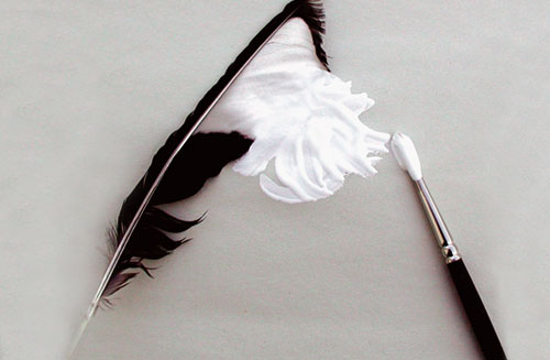 pincel pintando de blanco una pluma de pájaro