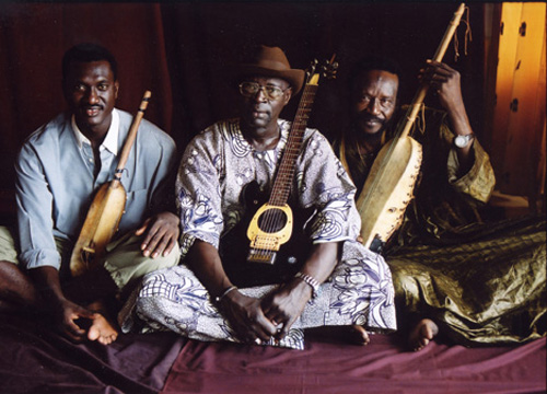 Ali Farka Toure, Bassekou Kouyate y Mama Sissoko sentados en el suelo posando con sus instrumentos musicales