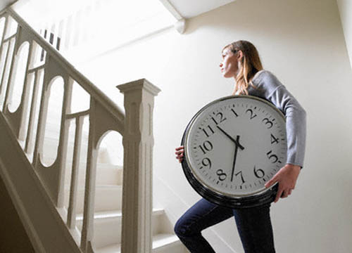 Mujer subiendo por las escaleras con un gran reloj entre las manos